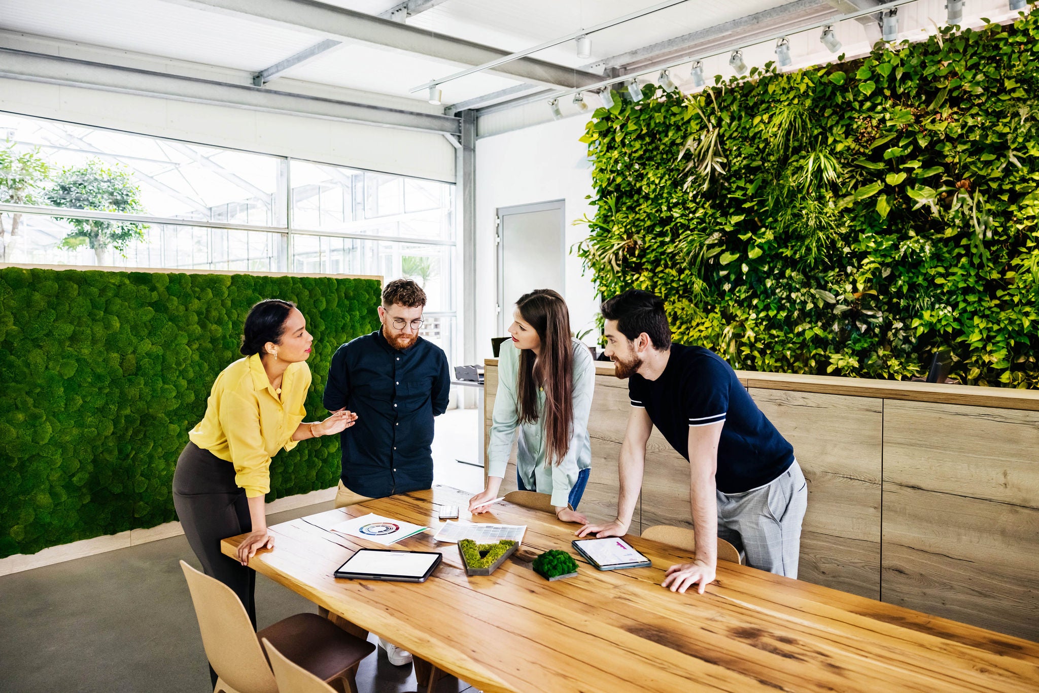 A group of  business associated huddled around a table having a serious meeting and sharing ideas in a green and modern office space.